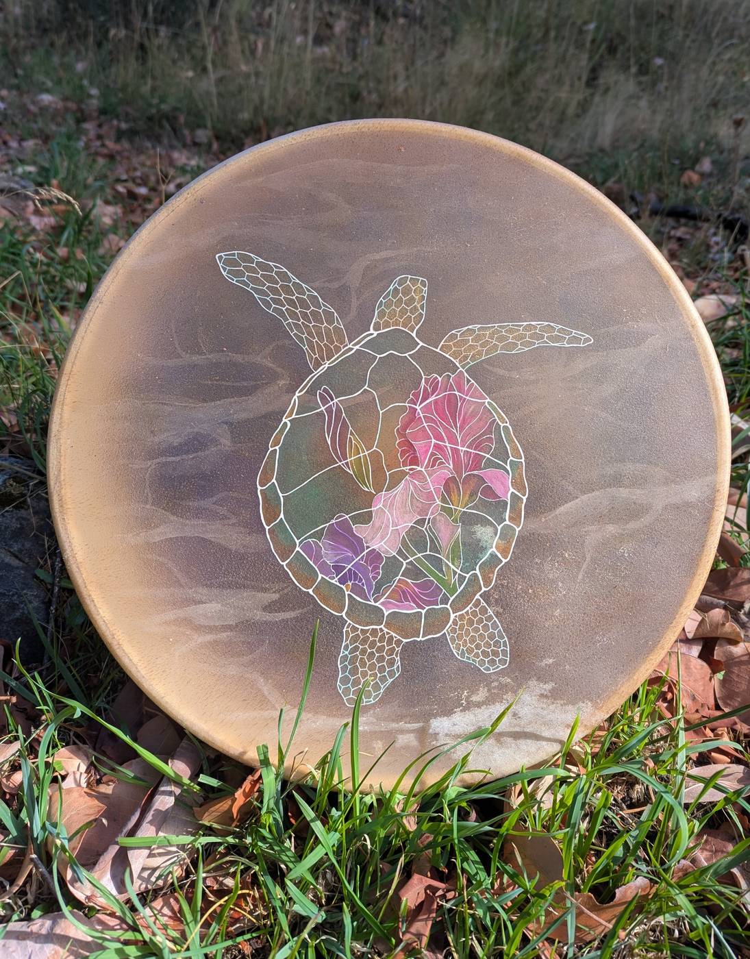 Hand drum painted with a sea turtle whose shell holds pink and purple irises